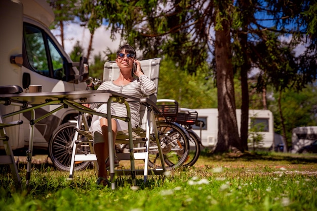 Vrouw praten op slimme telefoon buiten op een camping voor vakantiegangers. Caravan auto vakantie. Familie vakantiereizen, vakantiereis in camper RV. Verbinding informatie communicatie technologie.