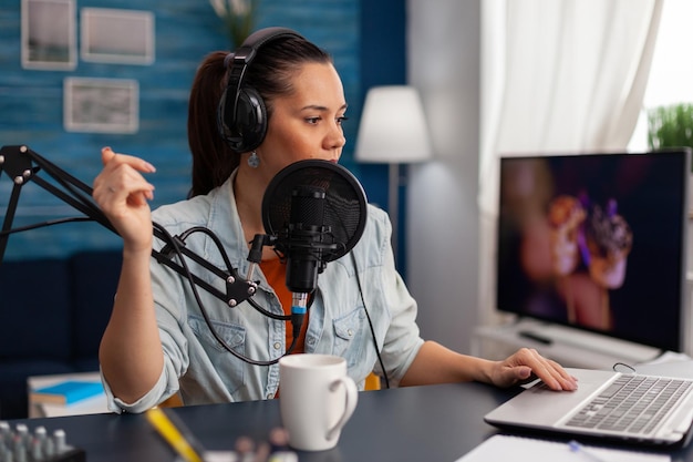 Vrouw praten over microfoon tijdens het gebruik van laptop. contentmaker met koptelefoon die podcast opneemt met audioapparatuur. social media influencer in thuiskantoor die live uitzendt.