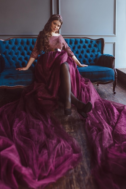 vrouw prinses (koningin) in lange paarse koninginnejurk en kroon zittend op de blauwe fluwelen sofa