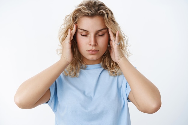 Foto vrouw probeert emoties onder controle te houden, voelt zich bedroefd en leeg, masseert de slapen met vingers en sluit de ogen om te ontspannen en te focussen, met hoofdpijn of migraine over een witte muur