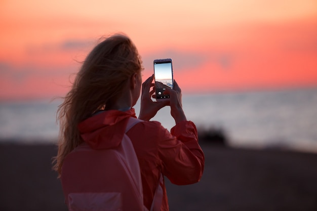 Vrouw reiziger met behulp van smartphone en het nemen van foto's van kleurrijke zee zonsondergang.