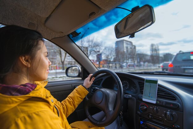 Vrouw rijdt auto bij koud winterweer, gebruik telefoon voor navigatie