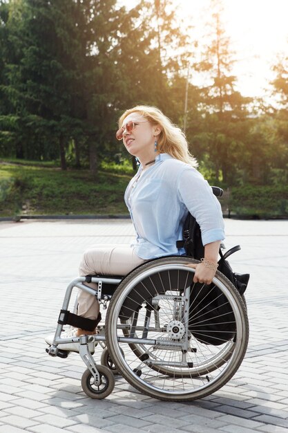 Vrouw rijdt een rolstoel op de weg in het zomer stadspark. Het concept van een toegankelijke omgeving voor mensen met een handicap.