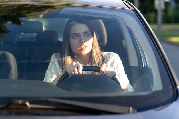 Vrouw rijdt voor het eerst in haar auto, probeert een auto-ongeluk te vermijden, is erg nerveus en bang, maakt zich zorgen, klampt zich stevig aan het stuur vast. Onervaren chauffeur in stress en verwarring na een ongeval