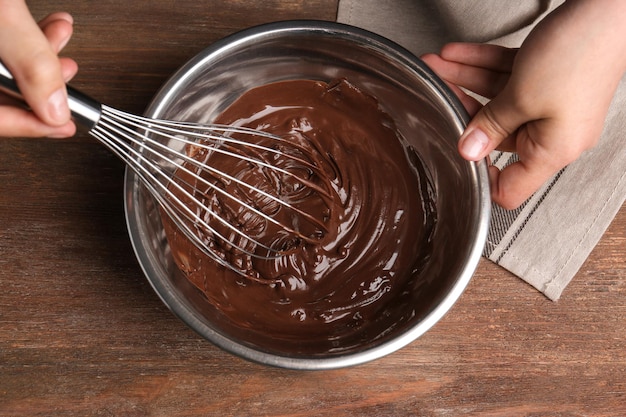 Vrouw roert heerlijke chocoladesaus in kom met garde op tafel