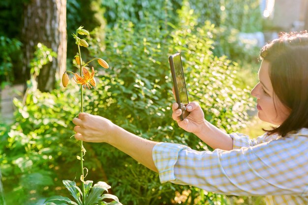 Vrouw rustend in de lentetuin fotograferen op smartphone bloeiende lelie plant