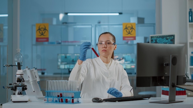 Vrouw scheikundige stof in reageerbuis analyseren voor wetenschappelijk experiment in laboratorium. Biologiespecialist met beschermende bril en handschoenen die kolf en laboratoriumglaswerk gebruiken voor innovatie.