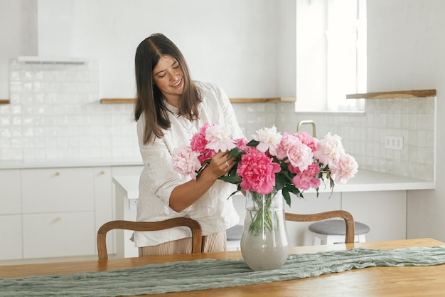 Vrouw schikken van mooie pioenrozen in vaas in nieuw modern huis