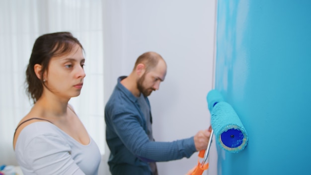 Vrouw schilderij muur met rolborstel tijdens het opknappen van de woonkamer van het appartement. paar samen opknappen. appartement herinrichting en woningbouw tijdens renovatie en verbetering. reparatie en de