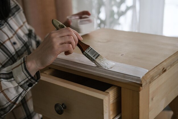 Foto vrouw schildert een houten nachtkastje met een borstel