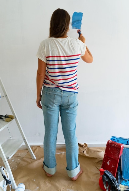 Vrouw schildert muur van haar flat in blauwe kleur doe-het-zelf huis renovatie concept