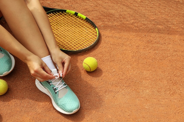 Vrouw schoenveters binden op gravel met racket en tennisballen