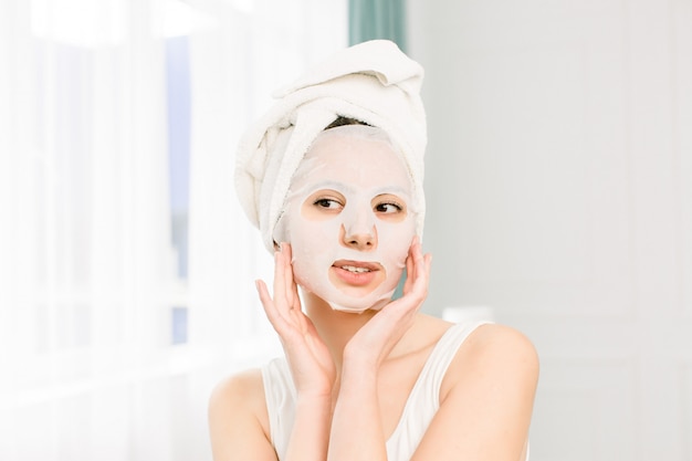 Vrouw schoonheid gezicht. Close-up van glimlachend jong wijfje die met Verse Natuurlijke Make-up Textielblad Gezichtsmasker toepassen. Portret van aantrekkelijke gelukkig meisje met witte cosmetische masker.