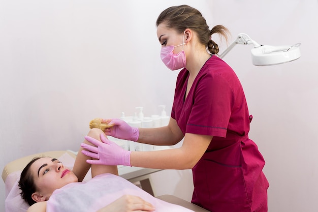 Vrouw schoonheidsspecialiste in speciale kleding, een beschermend masker en roze handschoenen maakt waxende handen van een jong meisje in een schoonheidssalon. Suikeren. Ontharen met een speciale suikerpasta