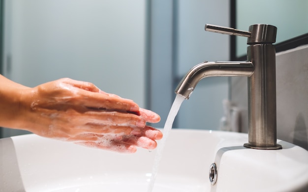 Vrouw schoonmaken en wassen van handen met zeep onder de kraan in de badkamer