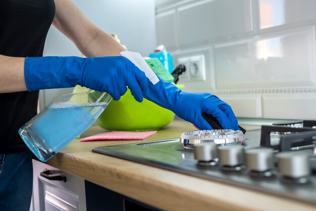 Vrouw schoonmaken van roestvrij staal gasoppervlak in de keuken met rubberen handschoenen.