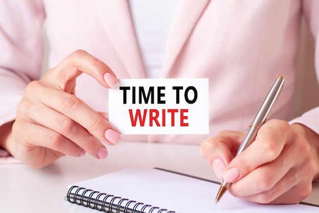 Vrouw schrijft in een notitieboekje met een zilveren pen en hand met kaart met tekst: TIME TO WRITE.