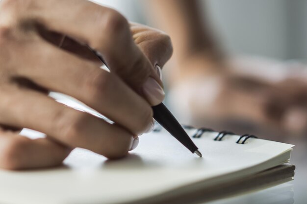 Foto vrouw schrijft met een pen in kladblok in een zonnig kantoorbedrijf en onderwijsconcept close-up