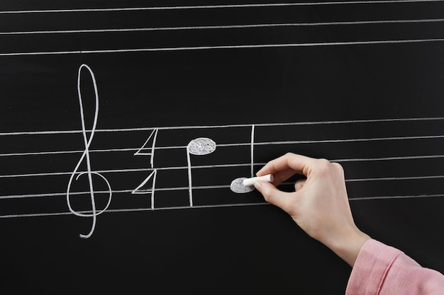Foto vrouw schrijft muzieknoten met krijt op blackboard close-up