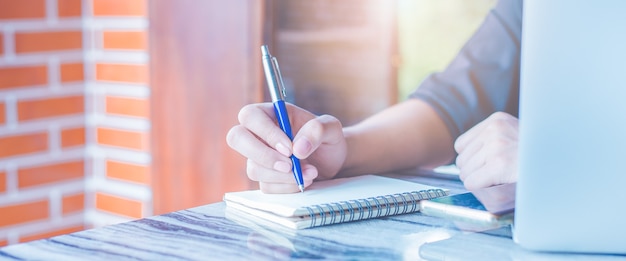 Vrouw schrijft op een notitieblok met een pen en ze gebruikt een mobiele telefoon op kantoor. Webbanner.