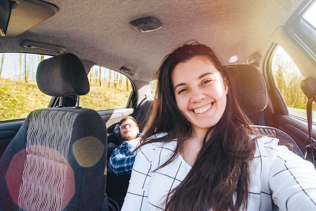 Vrouw selfie maken tijdens het autorijden met uitglijdende man op de achterbank. auto reisconcept