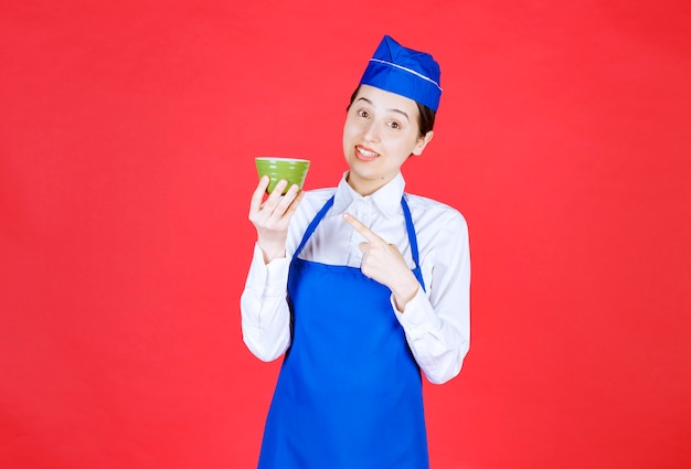 Vrouw serveerster in uniform staande en wijzend op een groene kom.