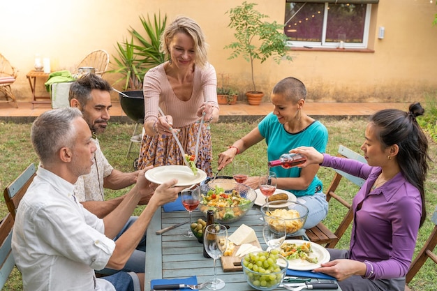 Vrouw serveert het eten met vrienden lachend buiten aan tafel