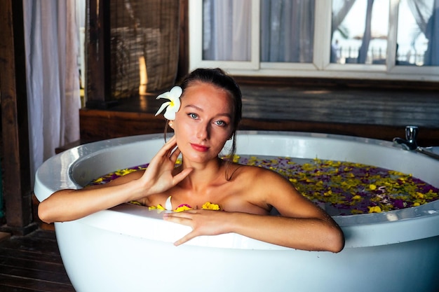 Vrouw sexy brunette ontspannen in bad met tropische bloemen buiten in luxe hotelresort. Biologische huidverzorging voor de huid. Mooi meisje rust in hotel spa massage en meditatie. vrouwendag 8 maart