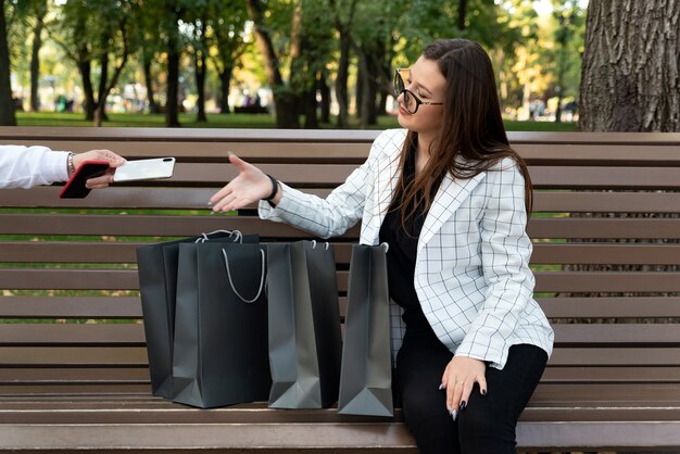 Vrouw shopper met boodschappentassen strekt zich uit haar hand voor de telefoon