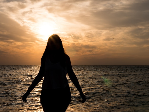 Foto vrouw silhouet kijken naar de zon op het strand bij zonsondergang... toeristisch meisje op strandvakantie