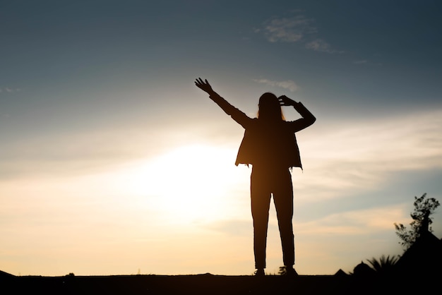 Vrouw silhouet staande hand opsteken op zonsondergang