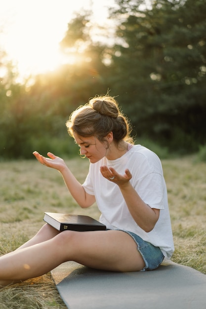 Vrouw sloot haar ogen biddend in een veld tijdens prachtige zonsondergang handen gevouwen in gebedsconcept voor ...