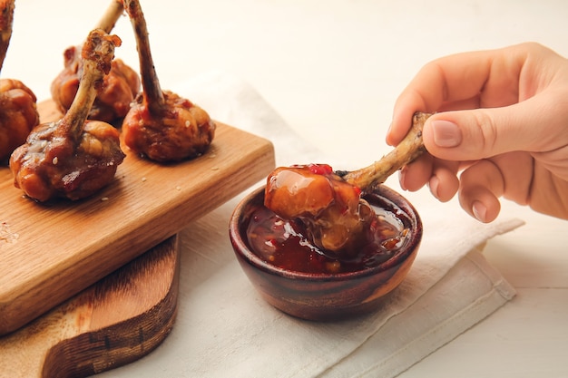 Vrouw smakelijke kip lollies met saus eten op lichte houten oppervlak