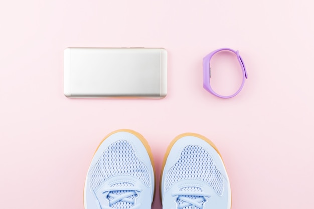 Vrouw sneakers, fitness tracker en smartphone op pastel roze achtergrond pastel