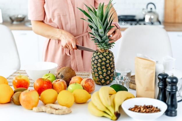 Vrouw snijden ananas Samenstelling van verschillende groenten en fruit op witte lichte keuken