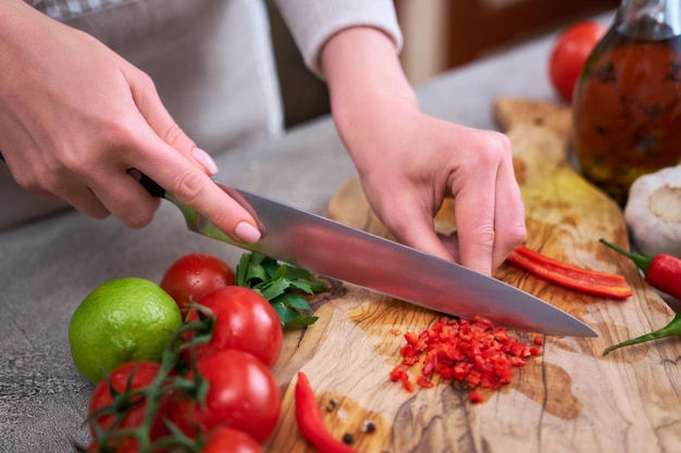 Vrouw snijden en chili peper met mes op houten bord