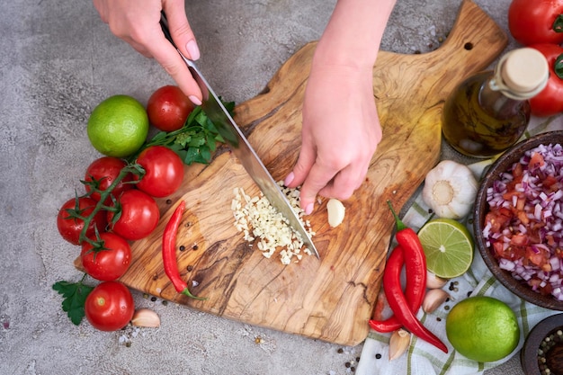 Vrouw snijden en hakken knoflook met een mes op een houten bord