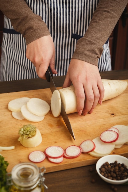 Vrouw snijden verse raap op een houten bord. Natuurlijk eten, gezonde dieetgroentesalade bereiden in de keuken, zijaanzicht