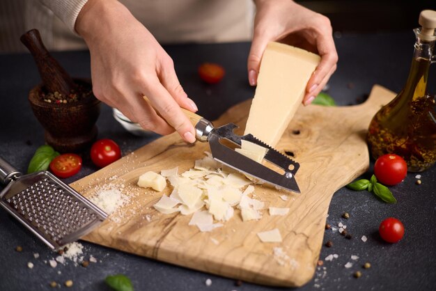 Vrouw snijdt een stuk traditionele Italiaanse parmesan harde kaas in vlokken op een houten snijstuk