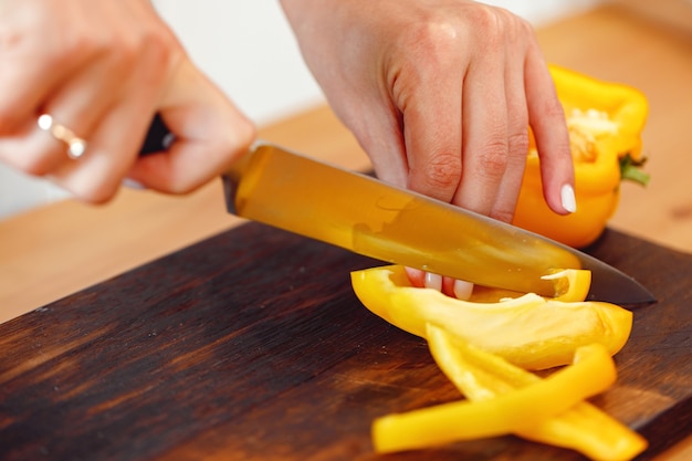 Vrouw snijdt gele paprika voor salade op houten tafel