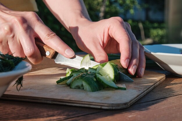 Vrouw snijdt komkommer op houten plank