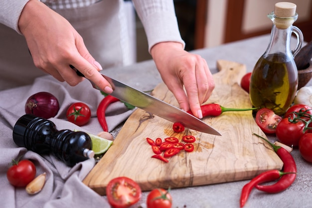 Vrouw snijdt verse rode chilipepers houten snijplank bij binnenlandse keuken