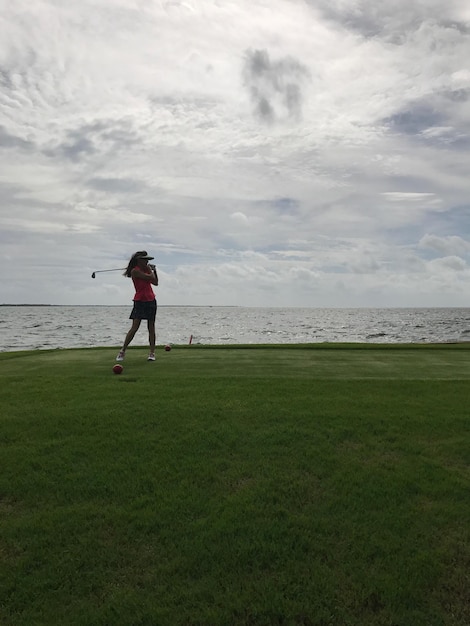 Foto vrouw speelt golf op een grasveld bij de zee tegen een bewolkte hemel