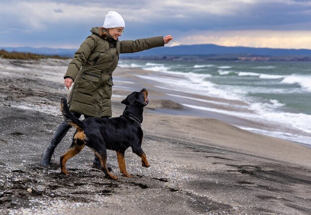 Vrouw speelt met rottweilerhond bij koud weer op het strand