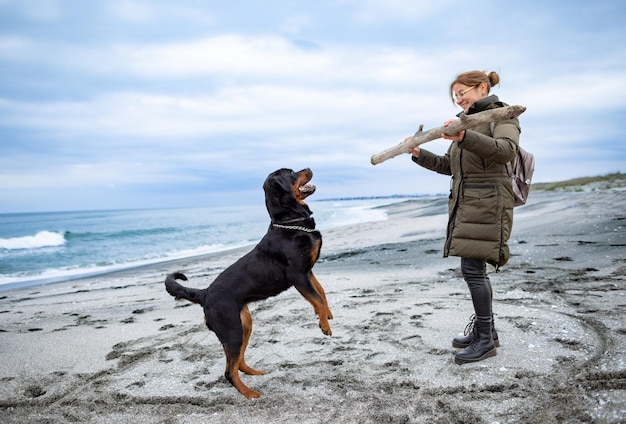 Vrouw speelt met rottweilerhond bij koud weer op het strand