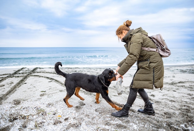 Vrouw speelt met rottweilerhond bij koud weer op het strand