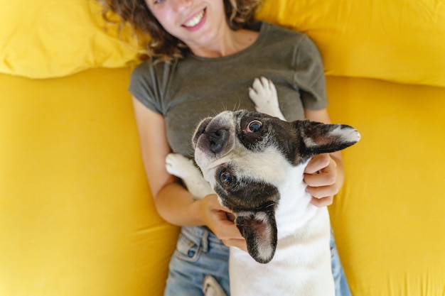 vrouw spelen met hond op gele achtergrond. Bovenaanzicht van hond in bed met onherkenbare vrouw die omhoog kijkt.