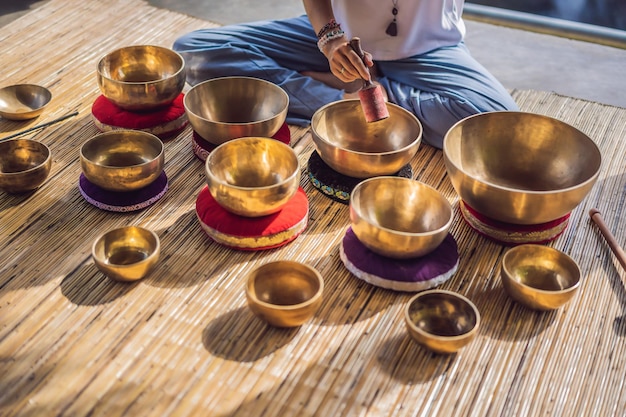 Vrouw spelen op Tibetaanse klankschaal zittend op yoga mat tegen een waterval Vintage toned mooi meisje met mala kralen mediteren