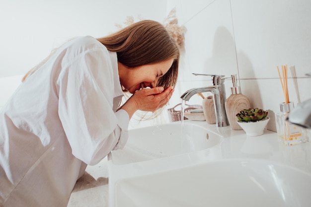Vrouw spettert gezicht met water over de wastafel in de badkamer