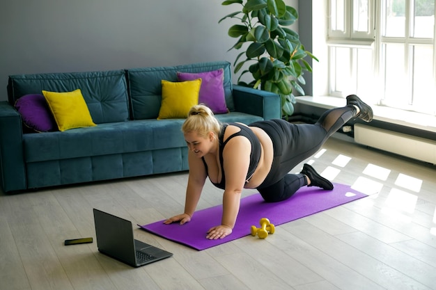 Vrouw sport online met een trainer thuis in de woonkamer en herhaalt oefeningen uit een video